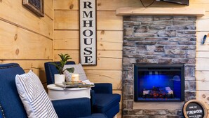 A cozy living room with a stone fireplace, a blue sofa, and a sign that reads "ARMHOUSE". - Enchanted Forest Hideaway by Ghosal Luxury Lodging (Sevierville)