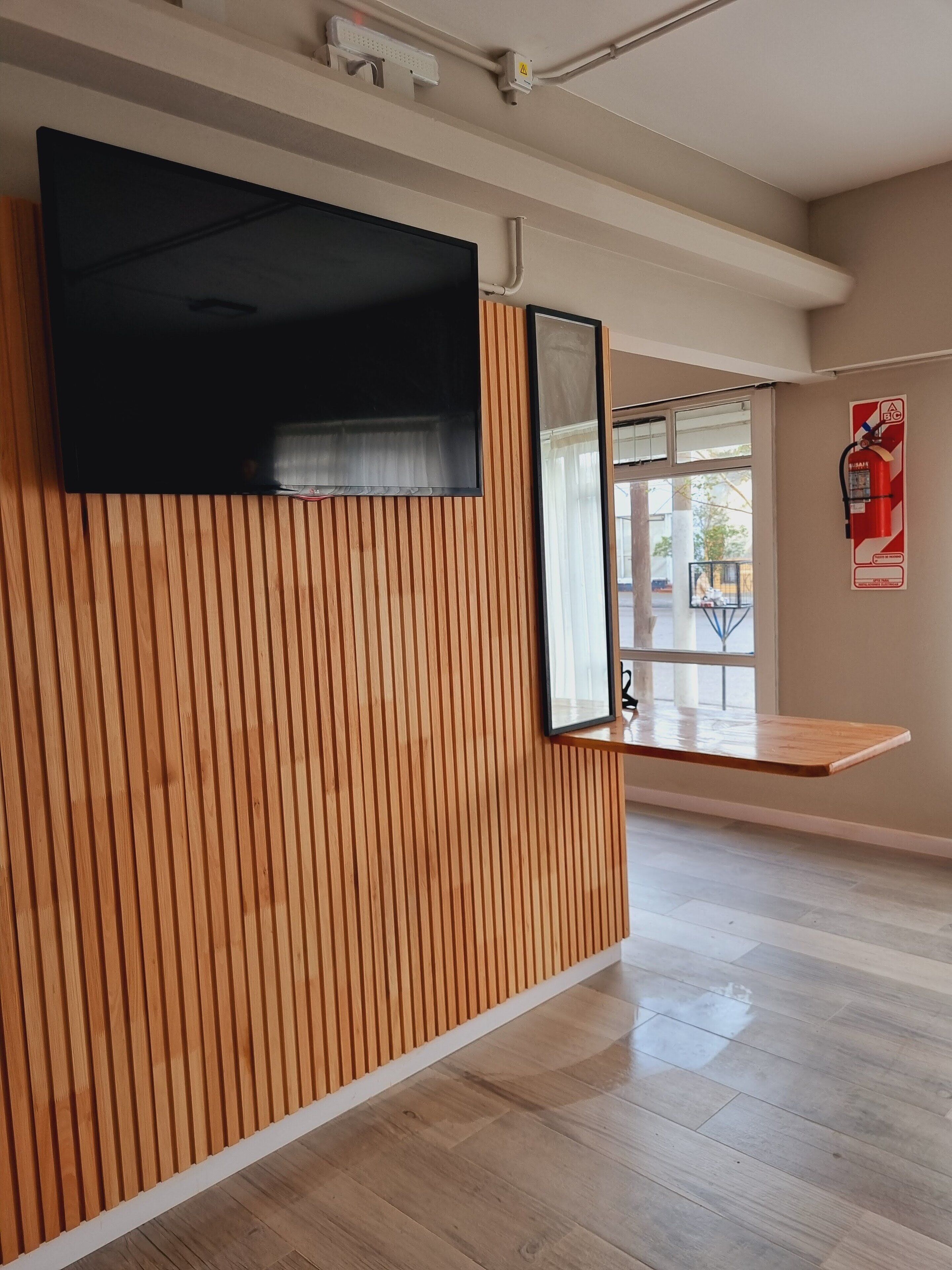 Un área de recepción moderna con un panel de madera en la pared, un televisor de pantalla plana montado, un espejo y un extintor en la pared.