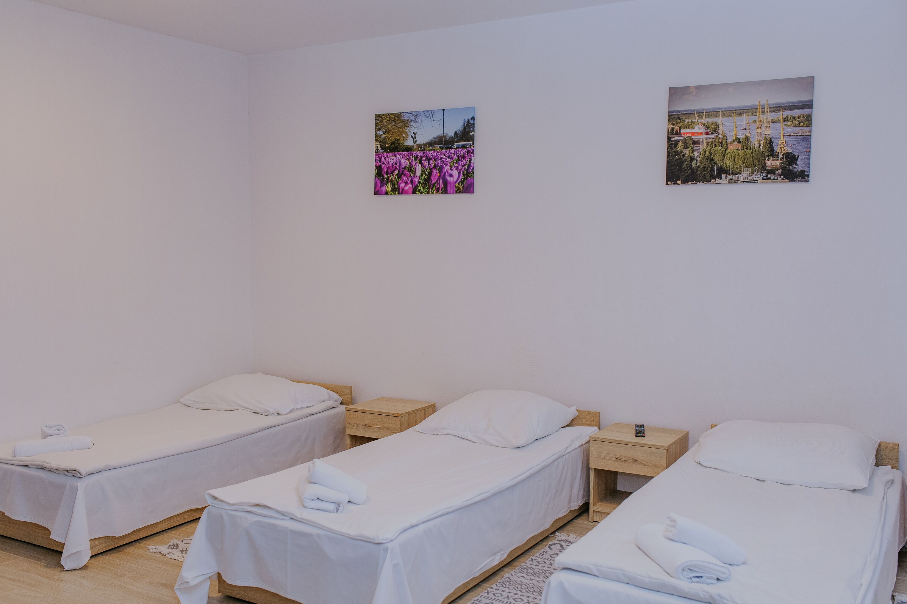 Ein Zimmer mit drei Einzelbetten, jeweils mit einem Holznachttisch und einem weißen Kopfkissen.