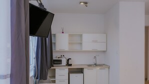 Een kleine keuken met witte kastjes, een magnetron, een waterkoker en een kleine koelkast.