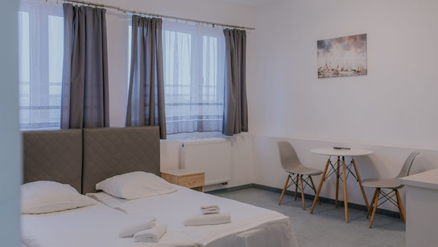 Een hotelkamer met een bed, een bureau, twee stoelen, een raam met gordijnen, en een schilderij aan de muur.