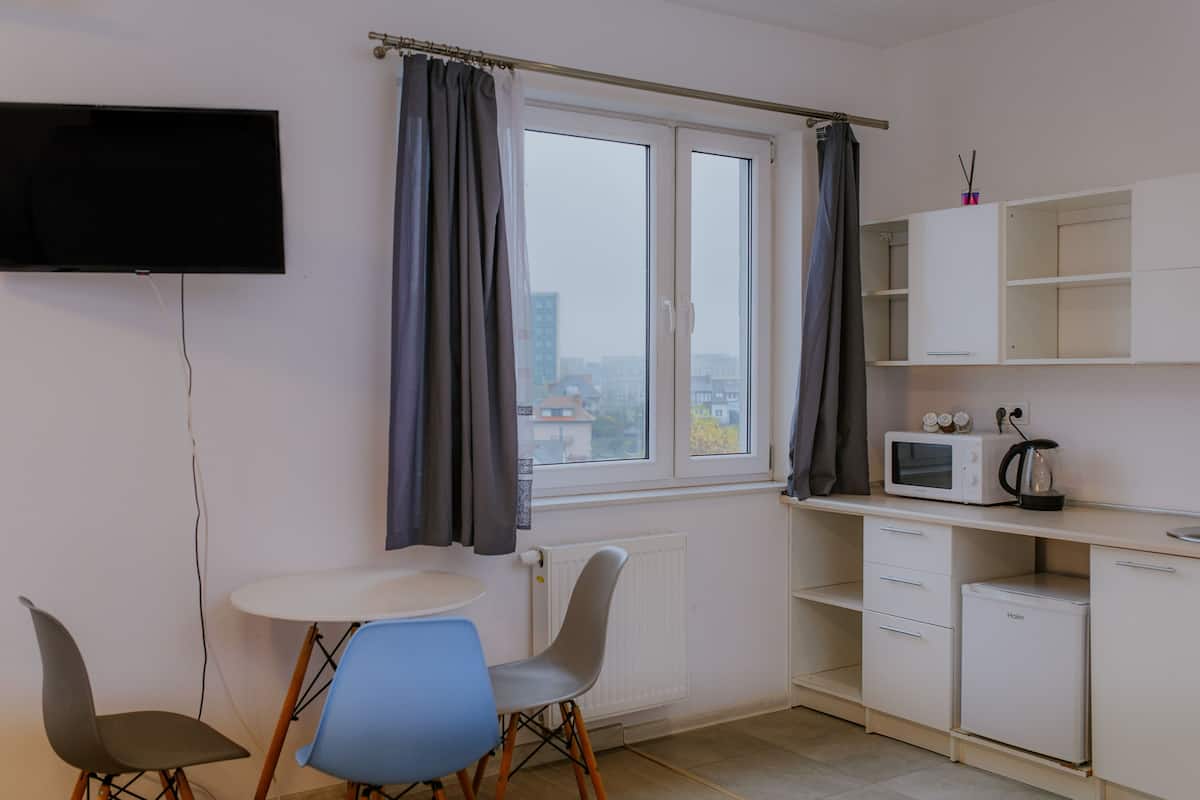Une petite cuisine équipée d’un micro-ondes, d’une bouilloire et de placards, d’un téléviseur fixé au mur et d’une fenêtre avec des rideaux.