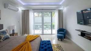 A modern hotel room with a bed, a blue armchair, a TV, and a sliding glass door leading to an outdoor area. - The Luxurious Chateau (Kingston)