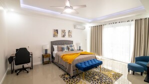 A modern bedroom with a bed, a desk, a chair, and a blue bench. - The Luxurious Chateau (Kingston)