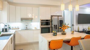 A modern kitchen with white cabinetry, a central island with seating, and pendant lighting. - The Luxurious Chateau (Kingston)