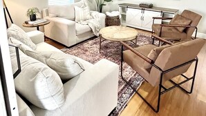 A living room with a white sofa, a brown armchair, a coffee table, a TV, and a ceiling fan. - “1933” Sleeps 6,  King Beds, Spacious, 5 min walk to downtown Mt. Dora  (Mount Dora)