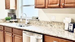 A kitchen with wooden cabinets, a stainless steel dishwasher, a granite countertop, and a window with blinds. - “1933” Sleeps 6,  King Beds, Spacious, 5 min walk to downtown Mt. Dora  (Mount Dora)