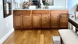 A kitchen with wooden cabinets, a countertop, and a dining area with a bench. - “1933” Sleeps 6,  King Beds, Spacious, 5 min walk to downtown Mt. Dora  (Mount Dora)