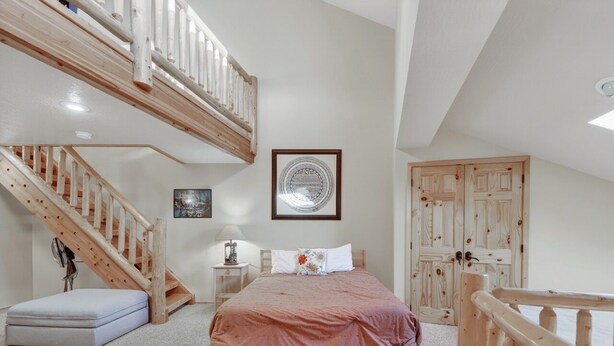 A bedroom with a wooden bed, a nightstand, a framed picture, a staircase, and a door. - Cozy 3-Level Condo w/ Loft Bedrooms w/ Fireplace (Brian Head)