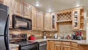 A kitchen with wooden cabinets, a black refrigerator, a microwave, a toaster, and a coffee maker. - Cozy 3-Level Condo w/ Loft Bedrooms w/ Fireplace (Brian Head)