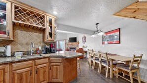 A spacious kitchen with wooden cabinets, a granite countertop, and a dining area with a wooden table and chairs. - Cozy 3-Level Condo w/ Loft Bedrooms w/ Fireplace (Brian Head)