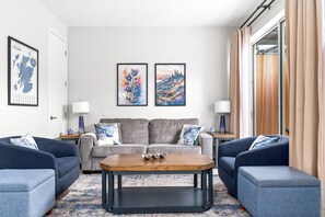 A modern living room with a sofa set, a coffee table, and two lamps. There are two framed artworks on the wall.