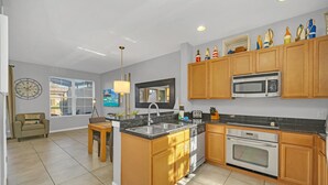 A modern kitchen with wooden cabinets, a built-in microwave, and a central island with a sink. - Waterfront/Minutes to Disney/Waterslides & Pool (Kissimmee)