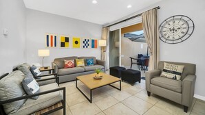 A modern living room with a sofa, armchair, and coffee table. There are abstract wall art pieces and a large clock. - Waterfront/Minutes to Disney/Waterslides & Pool (Kissimmee)