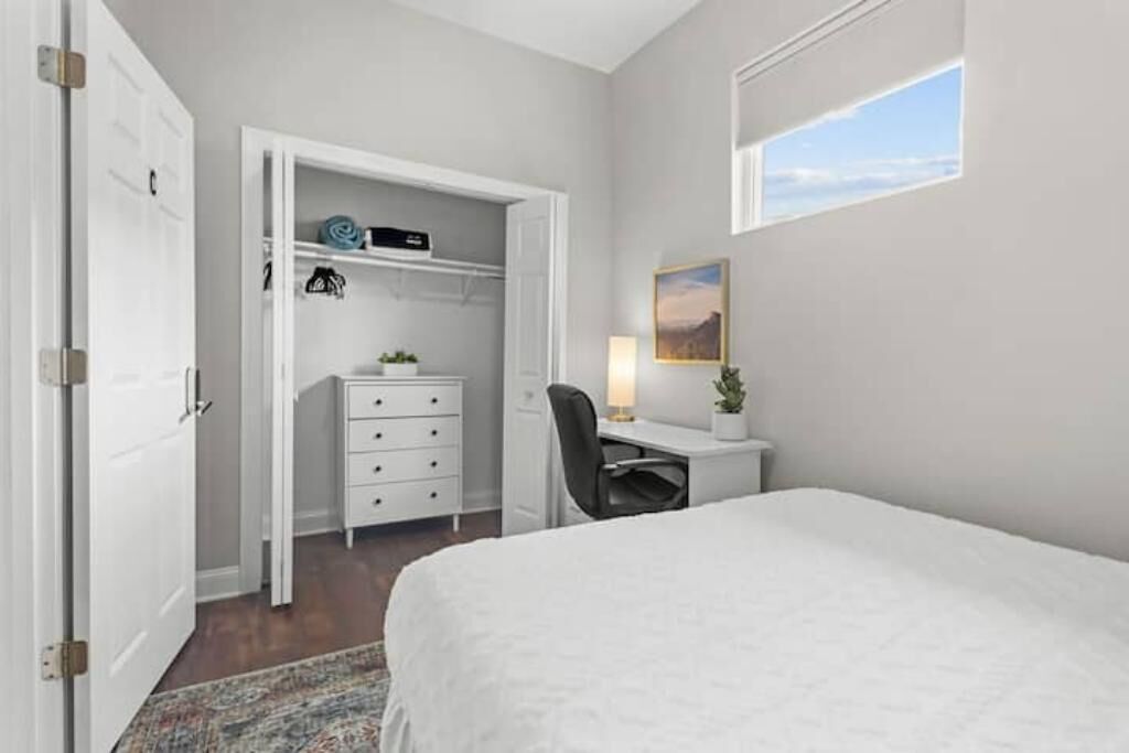 A bedroom with a bed, a desk, a chair, a wardrobe, and a window with a view.