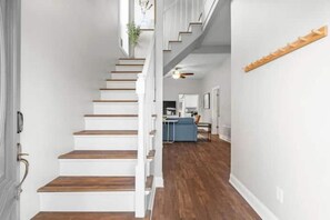 Una escalera con escalones de madera y paredes blancas que lleva a una zona de cocina.