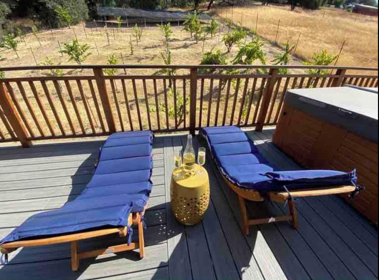Une terrasse avec deux chaises longues et une petite table, entourée d’une clôture en bois et d’un champ aride.