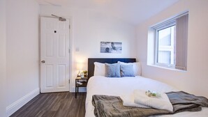 A bedroom with a bed, a nightstand, a lamp, a window, and a door.