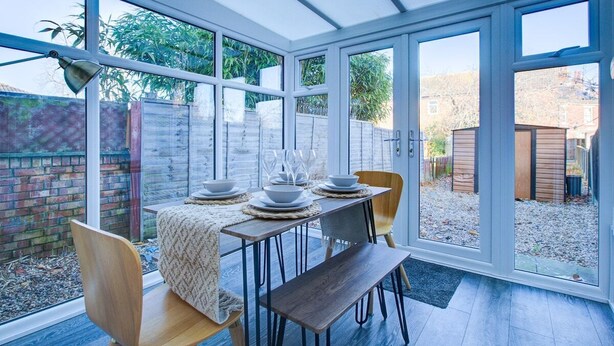 A conservatory with a dining table set for four, surrounded by glass doors and windows.