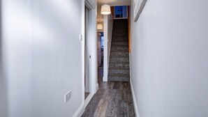 A narrow hallway with a wooden floor, white walls, and a staircase leading to an upper level.