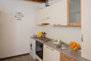 Een kleine keuken met een wasmachine, fornuis en een spoelbak. Er zijn kastjes en een aanrecht met verschillende keukenbenodigdheden.