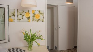 Een hal met een witte deur, een witte hanglamp en wanddecoratie met afbeeldingen van sinaasappels.