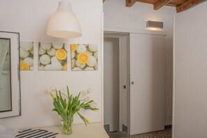 Un couloir avec une porte blanche, un luminaire suspendu blanc et des œuvres d’art murales représentant des oranges.