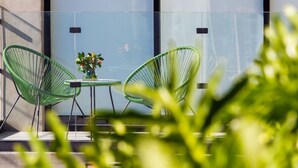 A balcony with two green chairs and a small table, a potted plant, and a glass wall. - KUKO SUITES (Chilpancingo de los Bravo)