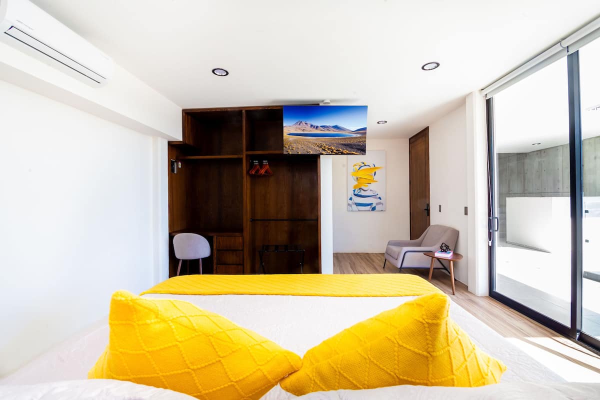 Un dormitorio moderno con cama, armario, silla y un amplio ventanal.