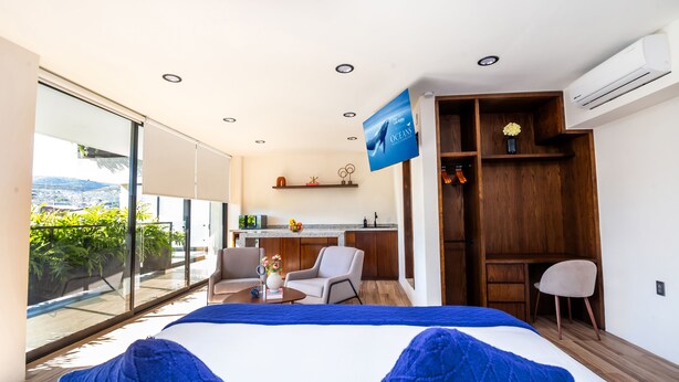 A modern hotel room with a large bed, a desk, a chair, and a balcony with a view of the city. - KUKO SUITES (Chilpancingo de los Bravo)