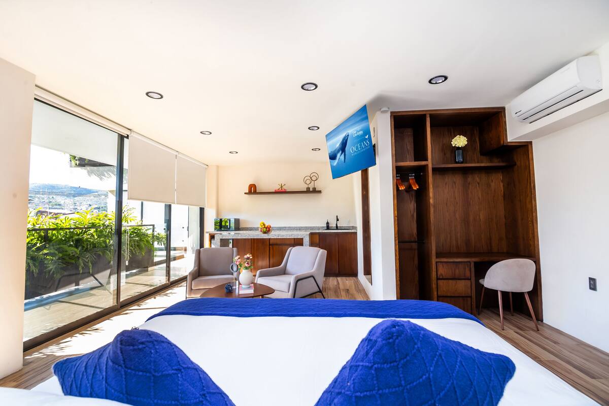 Una habitación de hotel moderna con una cama grande, un escritorio, una silla y un balcón con vista a la ciudad.