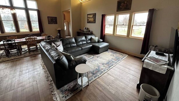 A spacious living room with a large sectional sofa, a dining area with a wooden table and chairs, and large windows providing natural light. - Parish & Bell Tower 18Ft ceilings and lots of space for guests. (Danbury)
