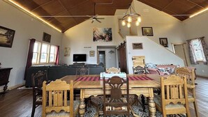 A spacious dining area with a high ceiling and exposed beams, a wooden dining table with chairs, and a staircase leading to an upper level. - Parish & Bell Tower 18Ft ceilings and lots of space for guests. (Danbury)