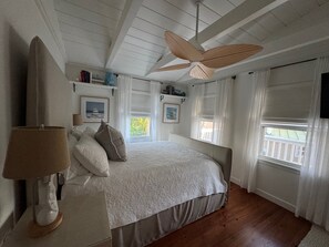 A bedroom with a bed, a ceiling fan, a lamp, and a window with curtains.