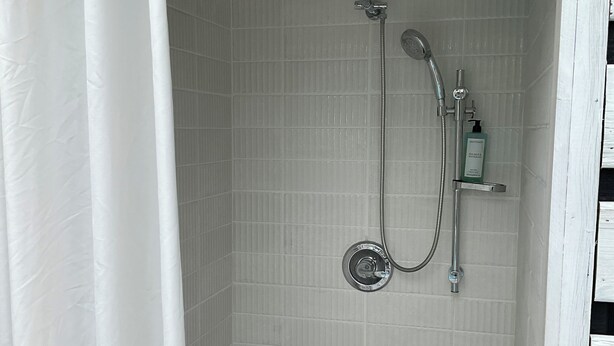 Eine Dusche mit Handbrause, Wandarmatur, Seifenspender und Duschvorhang.