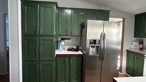 Une cuisine avec des armoires vertes, un réfrigérateur en acier inoxydable et un ventilateur de plafond.