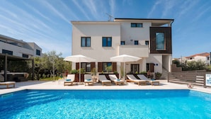 Ein modernes Gebäude mit Swimmingpool, Liegestühlen und Sonnenschirmen.