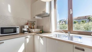 Eine moderne Küche mit weißen Schränken, einer Mikrowelle, einem Spülbecken und einem Fenster mit Blick auf Gebäude und Grünflächen.