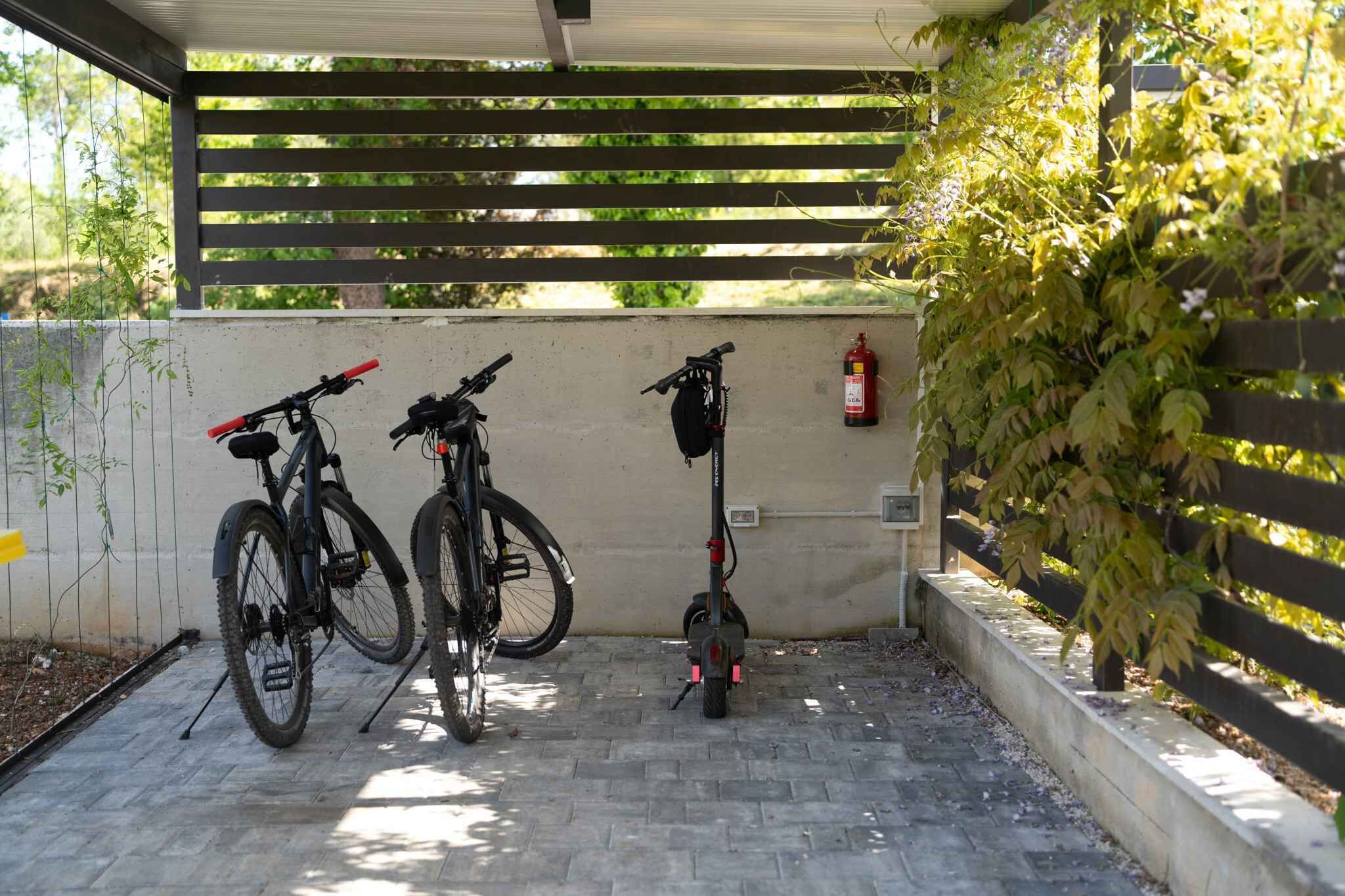 Ett takförsett utomhusområde med två cyklar och en elsparkcykel parkerade mot en vägg.