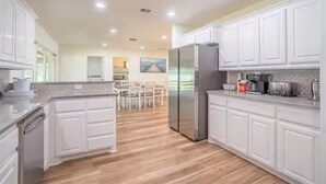 A modern kitchen with white cabinetry, a central island, and a dining area in the background. - Luxurious, fishing, riding boat and fun at Richland Chambers at Lake front home (Corsicana)