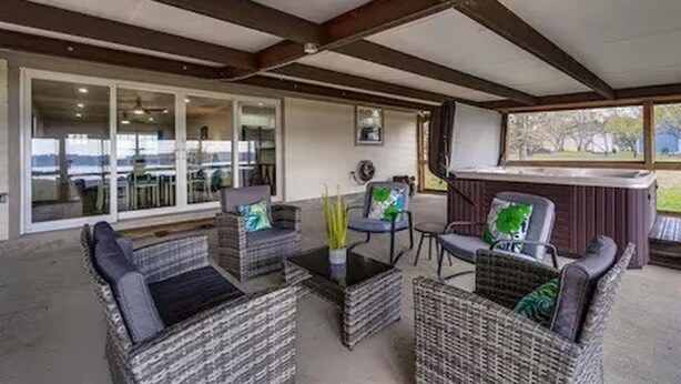 A covered outdoor seating area with wicker furniture and a hot tub. - Luxurious, fishing, riding boat and fun at Richland Chambers at Lake front home (Corsicana)