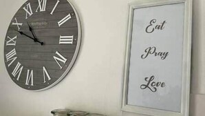 Eine Wanduhr mit römischen Ziffern und ein gerahmtes Schild mit der Aufschrift 'Eat Pray Love'.
