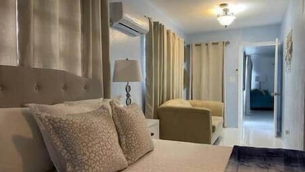Ein Hotelzimmer mit einem Bett, einem Sessel, einer Lampe und Blick auf den Flur.