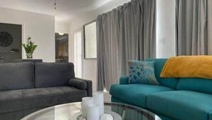 Ein modernes Wohnzimmer mit einem grauen Sofa, einem türkisfarbenen Sofa und einem Glastisch mit Kerzen.