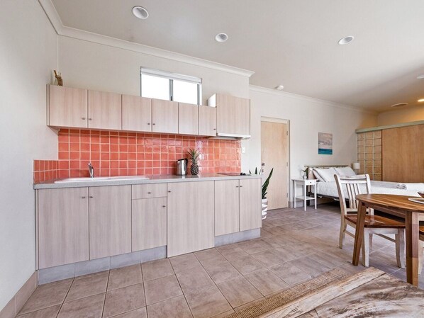 Una cocina moderna con armarios de madera clara, salpicadero rojo y una zona de comedor con mesa y sillas de madera.