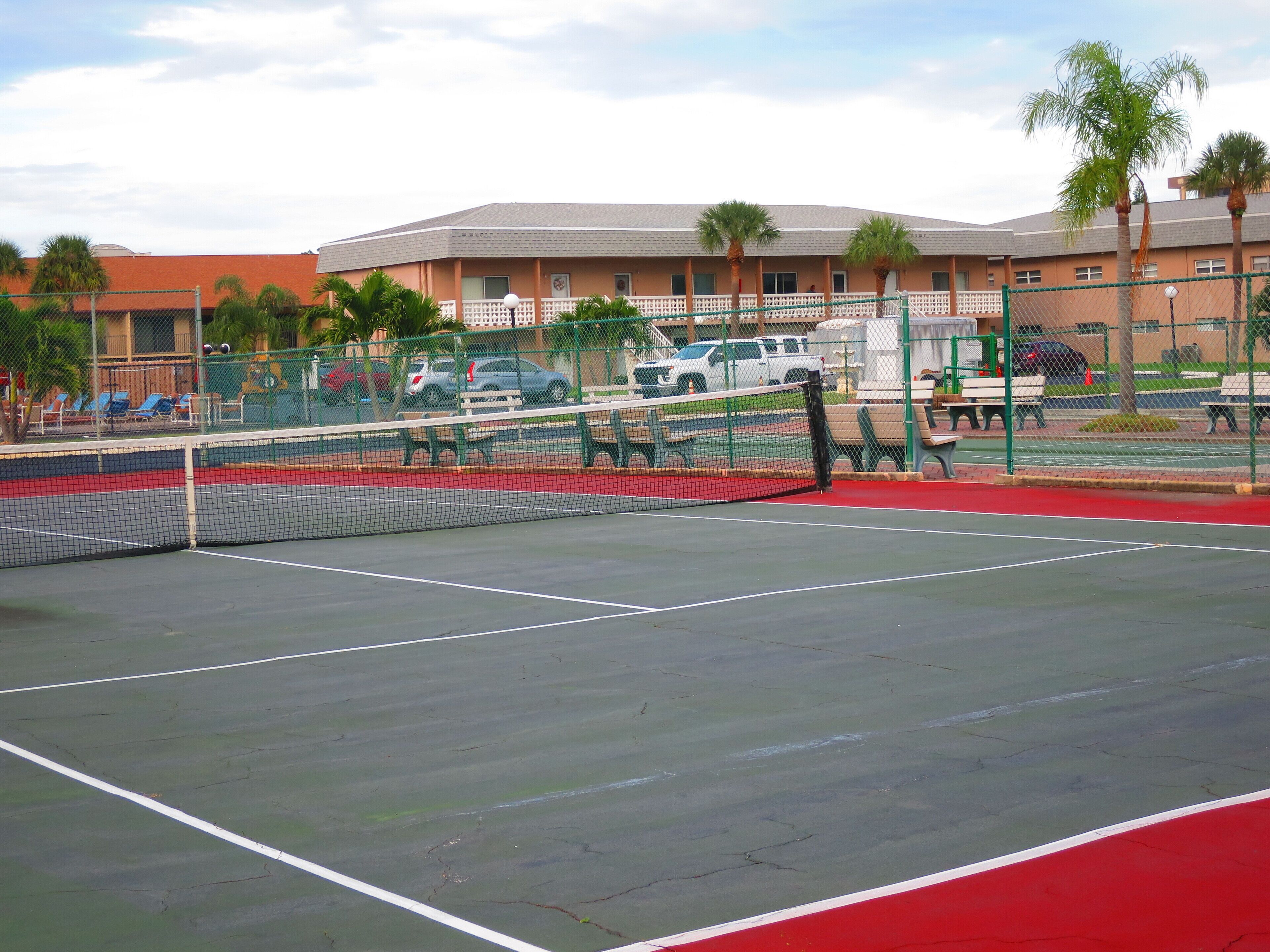 Una cancha de tenis con una red, rodeada por una valla y palmeras.