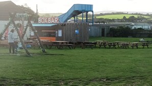 A rustic wooden structure with a blue staircase, picnic tables, and a sign reading "BOXBAR". - 3 bed Static 12ft Caravan Home From Home Somerset (Watchet)