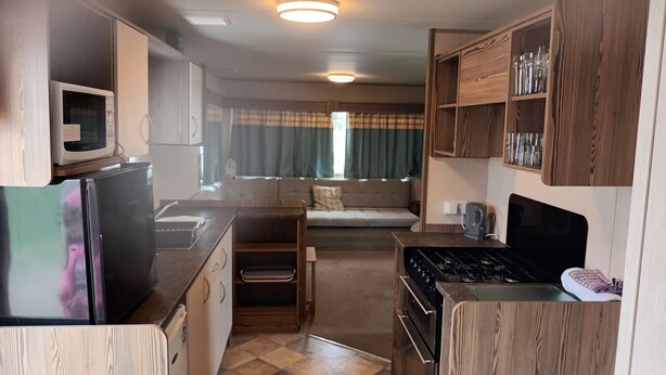 A compact RV kitchen with a stove, sink, and microwave. - 3 bed Static 12ft Caravan Home From Home Somerset (Watchet)
