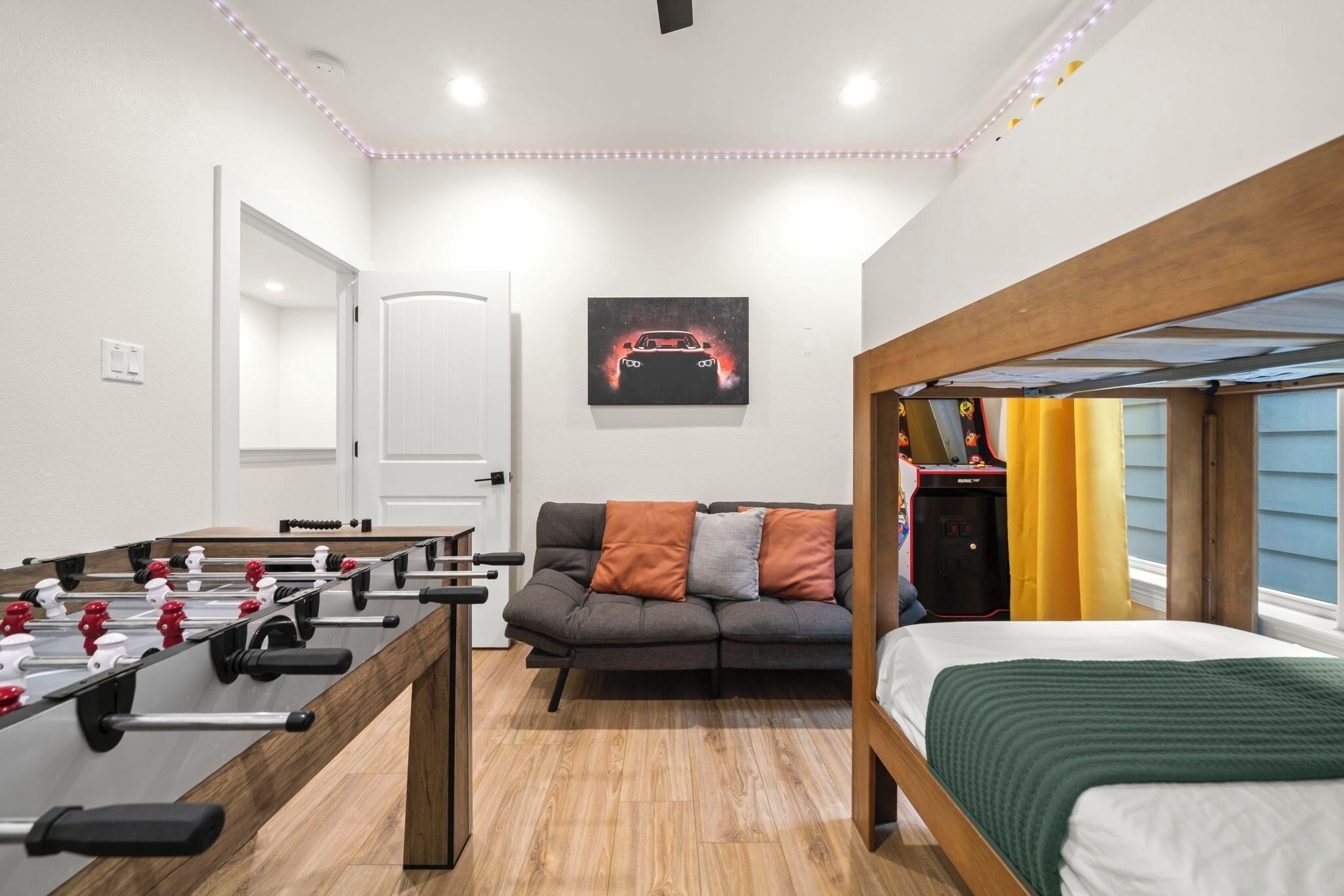 Una habitación con mesa de fútbol, sofá con cojines, cama y una obra de arte colgada en la pared.