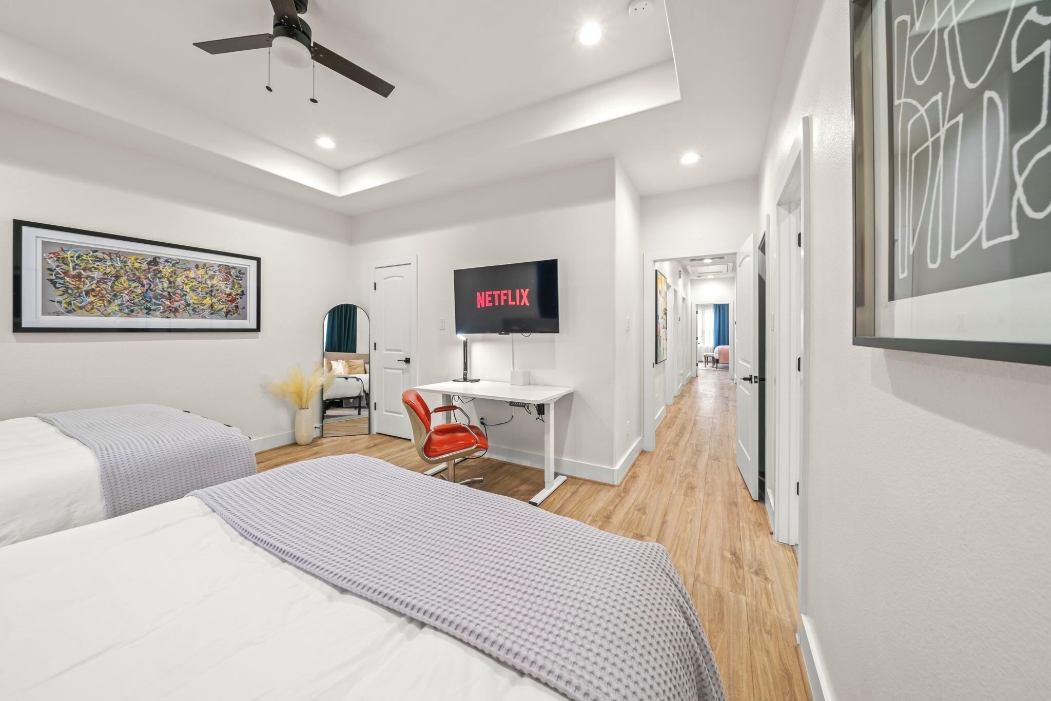 Una habitación de hotel moderna con una cama, un escritorio, una silla, un televisor y un pasillo.